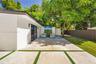 Concrete patio featuring inlaid synthetic turf strips, sliding glass doors, exterior wall-mounted lighting, and a fenced backyard with mature trees