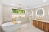 Freestanding soaking tub with gold-tone fixtures, walk-in glass-enclosed shower, wall-to-wall stone-style tile, wood-finish floating vanity with vesse