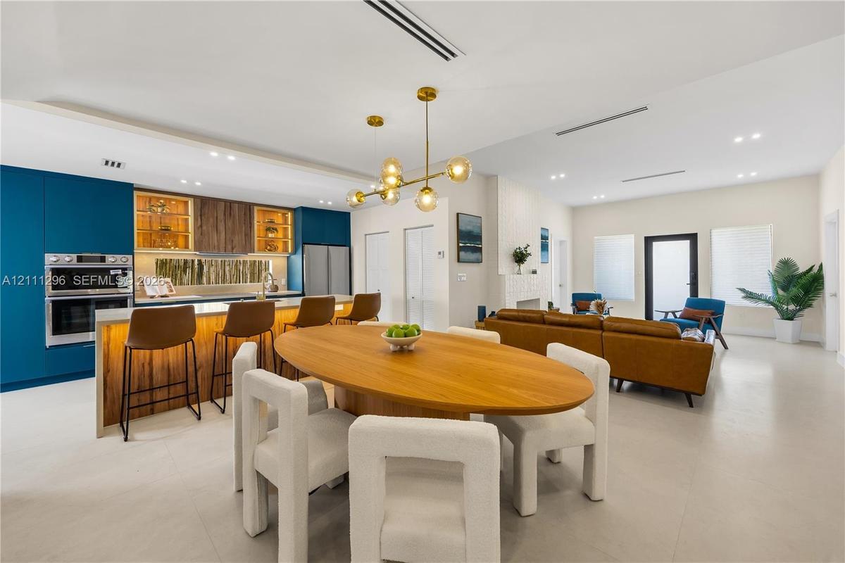 Modern kitchen featuring deep blue flat-panel cabinetry, integrated stainless steel double wall ovens, wood-finish accent shelving, a minimalist multi