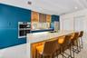 Kitchen featuring matte blue cabinetry, wood-finish upper cabinets with glass shelving, a large island with a stone-surface countertop, and built-in s