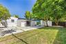 Backyard featuring a grass lawn, paved patio with inlay turf, mature trees, and enclosed wood fencing