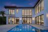 Rear of the residence at dusk with the illuminated pool and interiors aglow