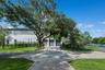 Stucco exterior featuring a three-car garage, stone-patterned concrete driveway, horizontal slat fencing, and mature oak trees