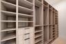 Custom wood-finish shelving unit featuring integrated drawer banks, adjustable open storage cubbies, vertical garment hanging rods, and matte black ha