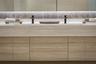 Floating wood-finish double vanity with stone countertop, integrated dual basins, matte black wall-mounted faucets, and polished stone backsplash with