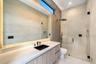 Floating vanity with wood-finish cabinetry, integrated LED mirror lighting, matte black fixtures, full-height tile wall detailing, and a glass-enclose