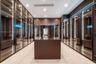 Custom dressing area featuring full-height glass-front cabinetry, integrated vertical LED accent lighting, wood-finish millwork, a matching central st