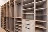 Custom walk-in closet system featuring wood-finish cabinetry, extensive adjustable shelving, integrated hanging rods, and drawers with matte black har
