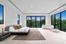 Open-concept room featuring floor-to-ceiling glass panel walls with black frames, recessed tray ceiling, neutral stone-finish flooring, and integrated