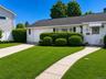 White siding exterior with a dark shingle roof, complemented by a concrete driveway and walkway
