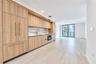 Kitchen featuring custom wood-finish cabinetry, stone-patterned backsplash, integrated appliances, brass-tone hardware, and large-format tile flooring