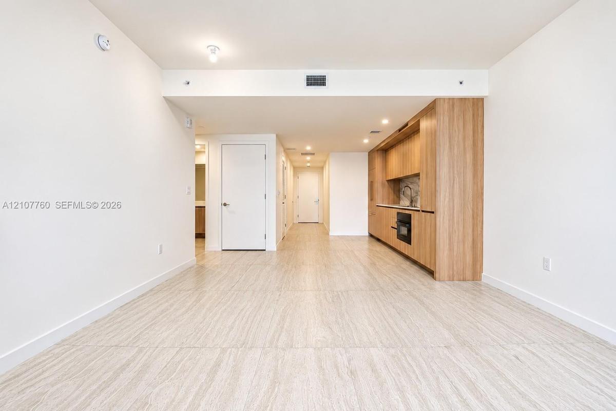 Open-concept interior featuring wood-finish flooring, custom wood-veneer cabinetry, stone backsplash, recessed lighting, and integrated wall oven