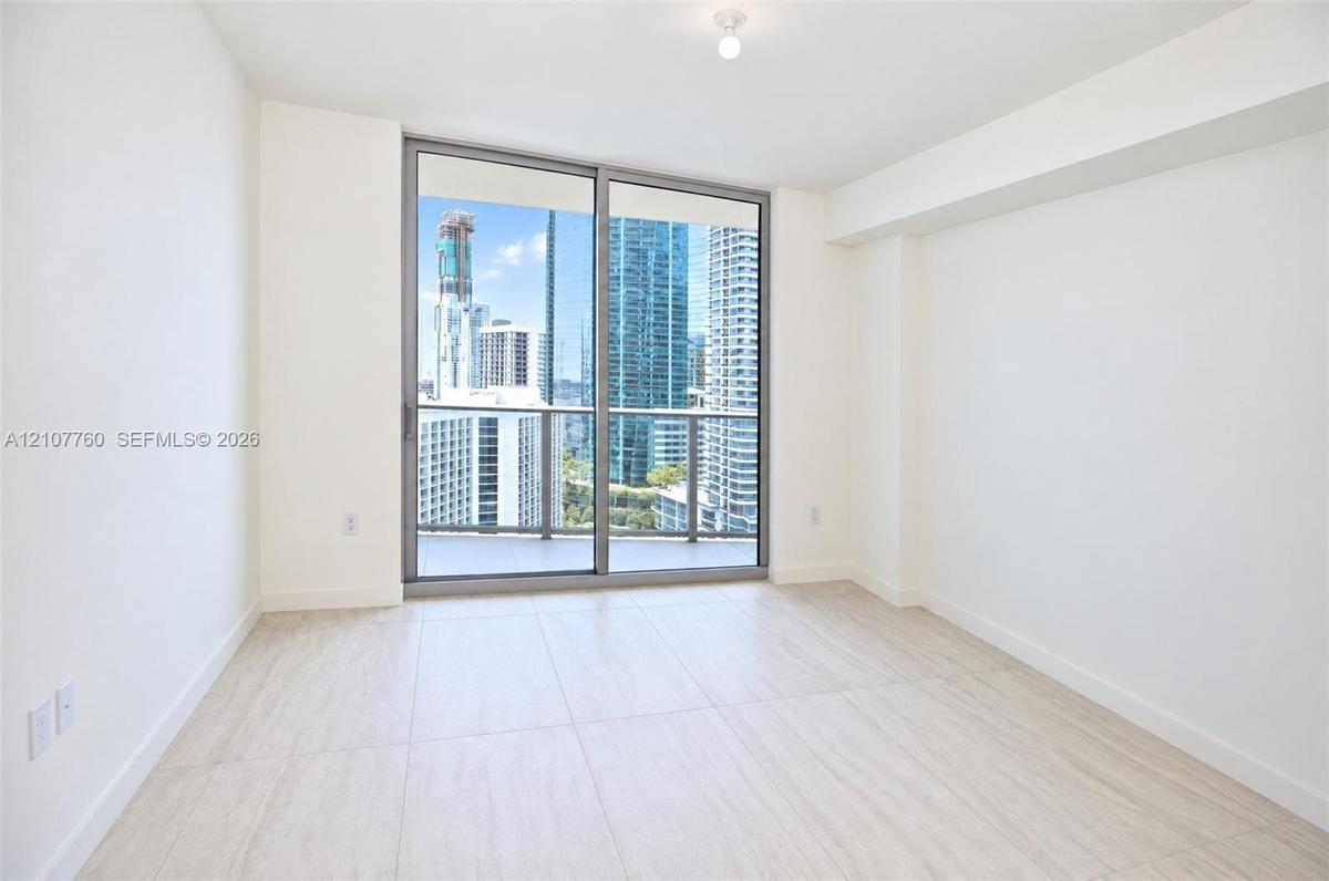 Floor-to-ceiling sliding glass doors, neutral tile flooring, and urban skyscraper scenery