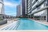 Outdoor lap pool featuring tiled steps, stone-finish decking, glass panel railings, and metal pergolas