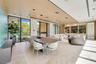 Modern open-concept interior featuring light wood-finish cabinetry, floor-to-ceiling glass sliding walls, stone-finished kitchen island, recessed ligh
