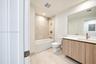 Bathroom featuring a wood-finish floating vanity, neutral-toned tile flooring, large wall-mounted mirror, and a tub with tiled surround and bronze-ton