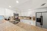Kitchen featuring white shaker-style cabinetry, expansive stone countertops, stainless steel appliances, a double-basin undermount sink, and mirrored 