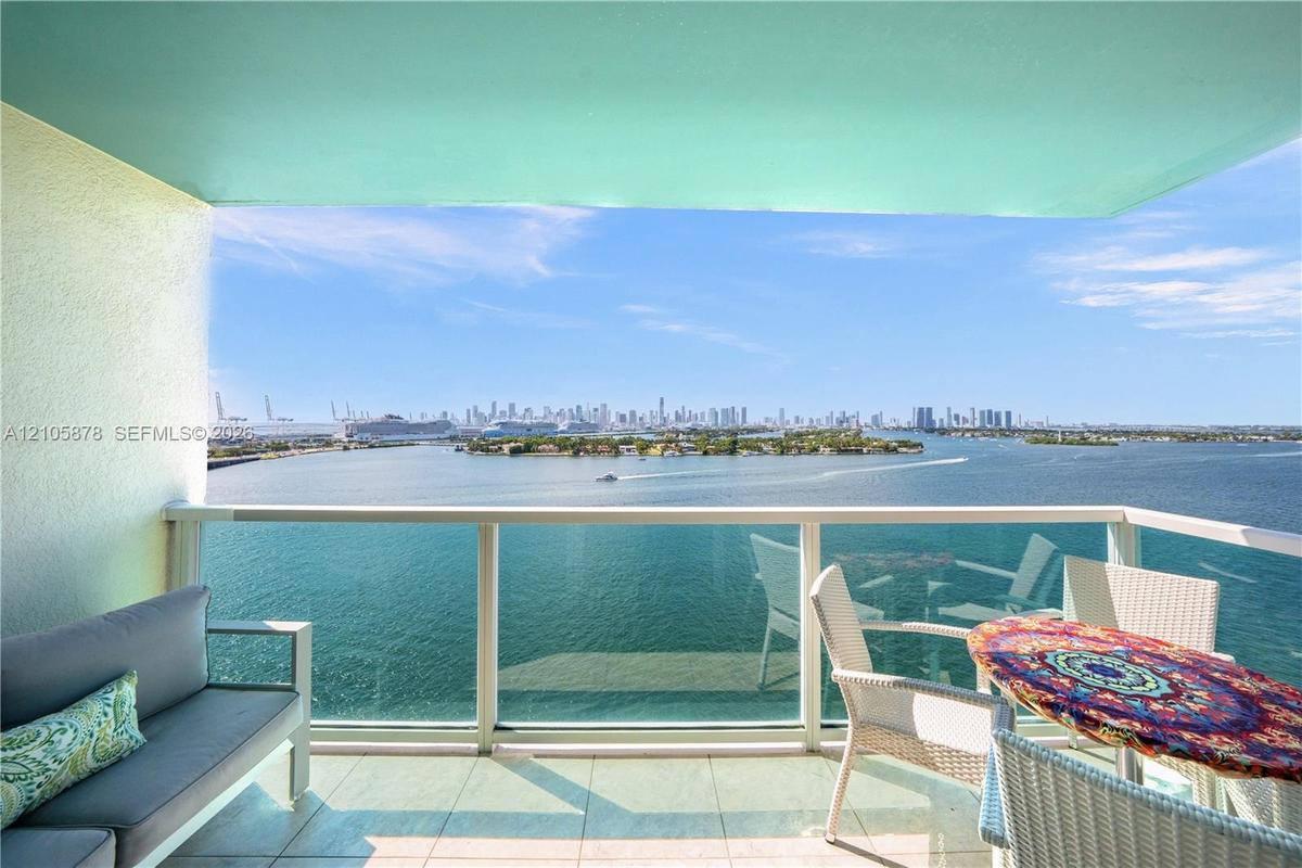 Private balcony featuring tiled flooring, structural overhang, and a glass-paneled railing overlooking the harbor and city skyline