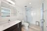 Dark-finish floating vanity with a white countertop and rectangular integrated sink, walk-in shower with white subway tile surround and glass enclosur