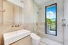 Modern bathroom featuring a wood-finish floating vanity, wall-mounted metallic fixtures, a frameless glass shower enclosure, large-format stone tiling