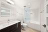 Bathroom featuring a dark-finish wood vanity with a white countertop, subway-tiled shower surround with a glass panel, and light-toned tile flooring