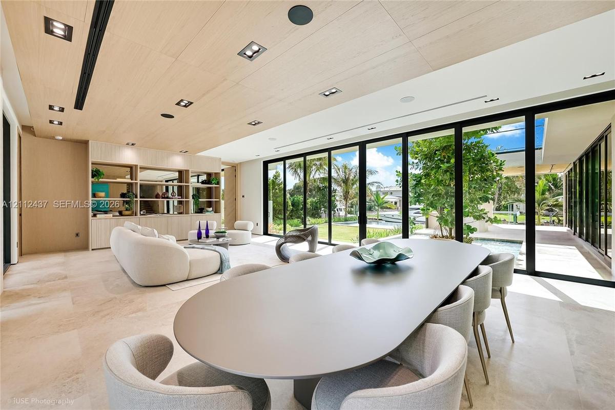 Open-concept interior featuring light wood-panel ceilings, large-format stone flooring, floor-to-ceiling glass sliding doors, and integrated recessed 