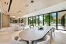 Open-concept interior featuring light wood-panel ceilings, large-format stone flooring, floor-to-ceiling glass sliding doors, and integrated recessed 