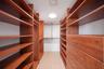 Walk-in storage space featuring extensive custom wood-finish shelving, integrated clothing rods, built-in dresser drawers with metallic pulls, and lig