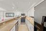 Kitchen featuring white cabinetry, stone countertops, stainless steel appliances, a double-basin sink, and tile flooring