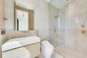 Floating vanity with integrated sink, glass-enclosed walk-in shower, wall-mounted brushed metal plumbing fixtures, and textured stone wall tile