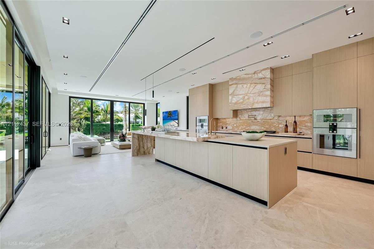 Floor-to-ceiling retractable glass walls, light wood-paneled ceiling with integrated recessed lighting, expansive stone flooring, and custom built-in 