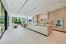 Floor-to-ceiling retractable glass walls, light wood-paneled ceiling with integrated recessed lighting, expansive stone flooring, and custom built-in 