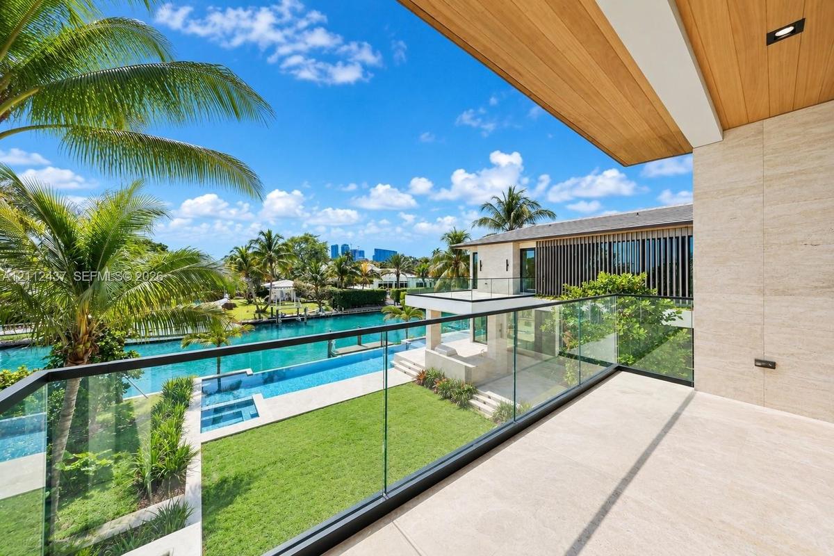 Covered balcony featuring stone flooring, wood-plank ceiling, and a frameless glass railing overlooking the waterfront property, swimming pool, and la