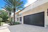 Modern exterior featuring stone facade cladding, large-format paved driveway, sleek roll-down garage door, and glass balcony railings