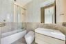 Bathroom featuring a floating vanity with a white countertop, wall-mounted faucet, glass-enclosed soaking tub with stone tile surround, and textured w