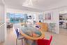 Open-concept interior featuring light wood-finish flooring, floor-to-ceiling glass sliding doors, recessed tray ceiling lighting, and a modern sculptu