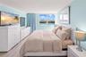 Bedroom featuring light-toned wood-finish flooring, a large window with cityscape and water scenery, and a bright, neutral color palette