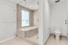 Bathroom featuring a frameless glass-enclosed tub with floor-to-ceiling tile surround, neutral-toned large-format tile flooring, and a white porcelain