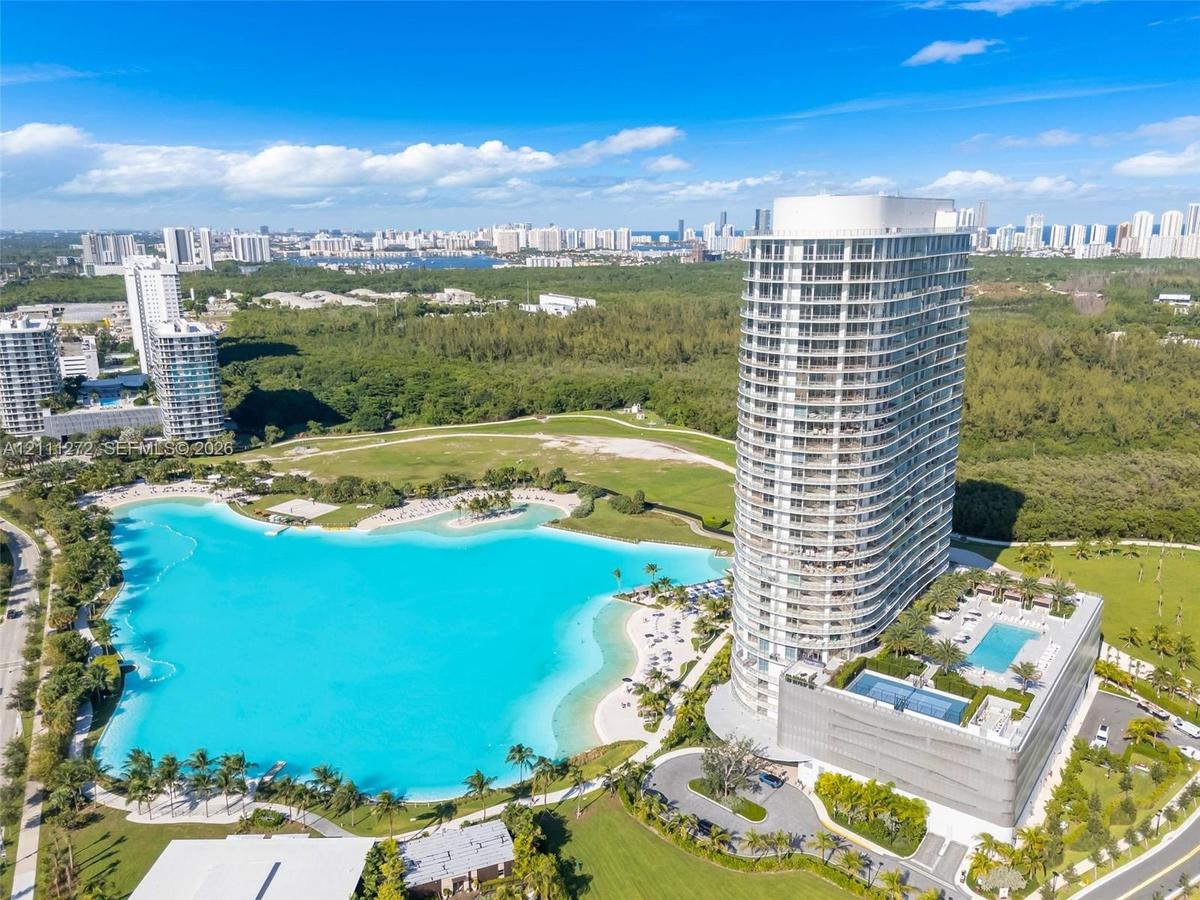 High-rise residential tower featuring a multi-level podium, rooftop swimming pool, expansive turquoise lagoon, and surrounding manicured green space
