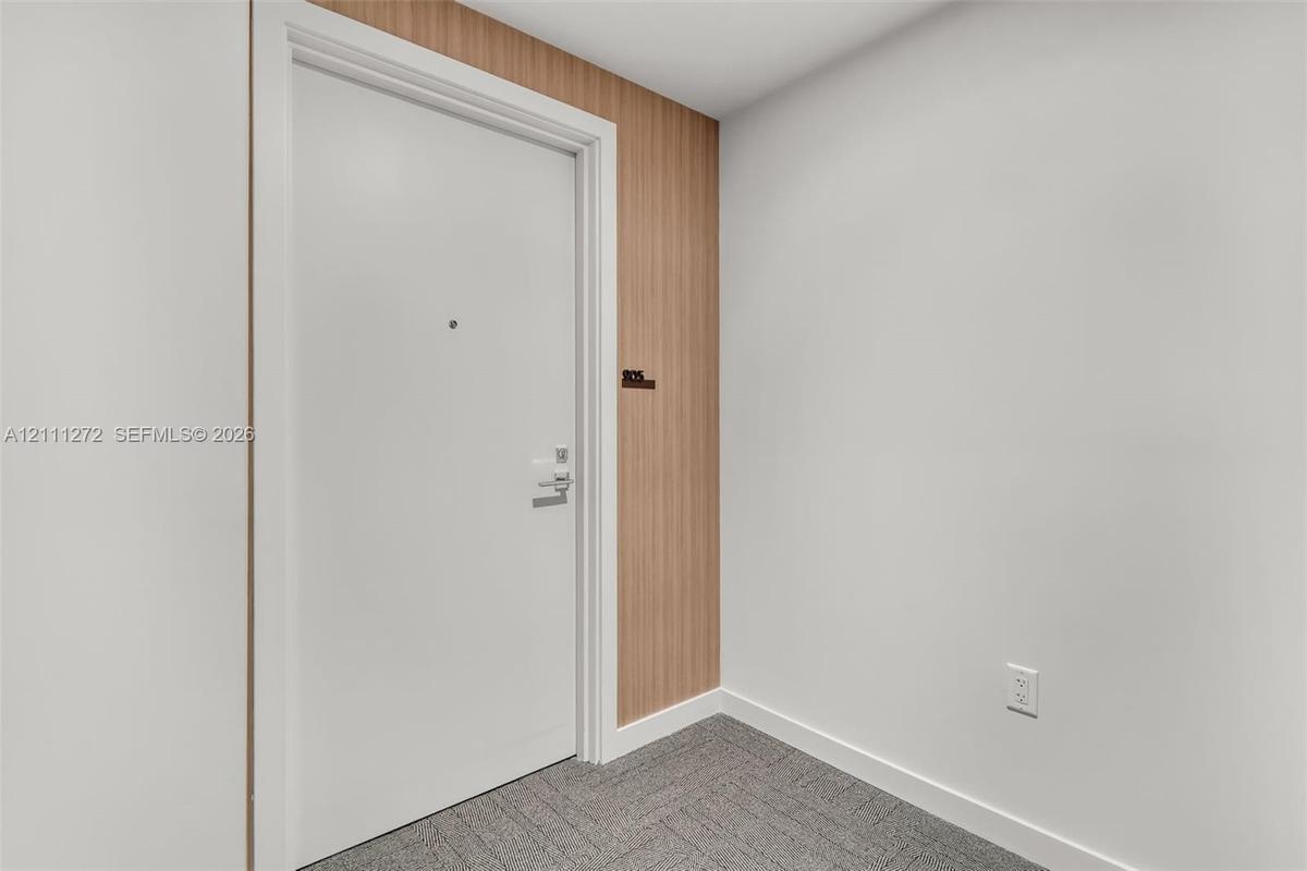 Entryway featuring a solid door with integrated peephole and metal hardware, accent wall with vertical wood-finish paneling, and neutral carpeting