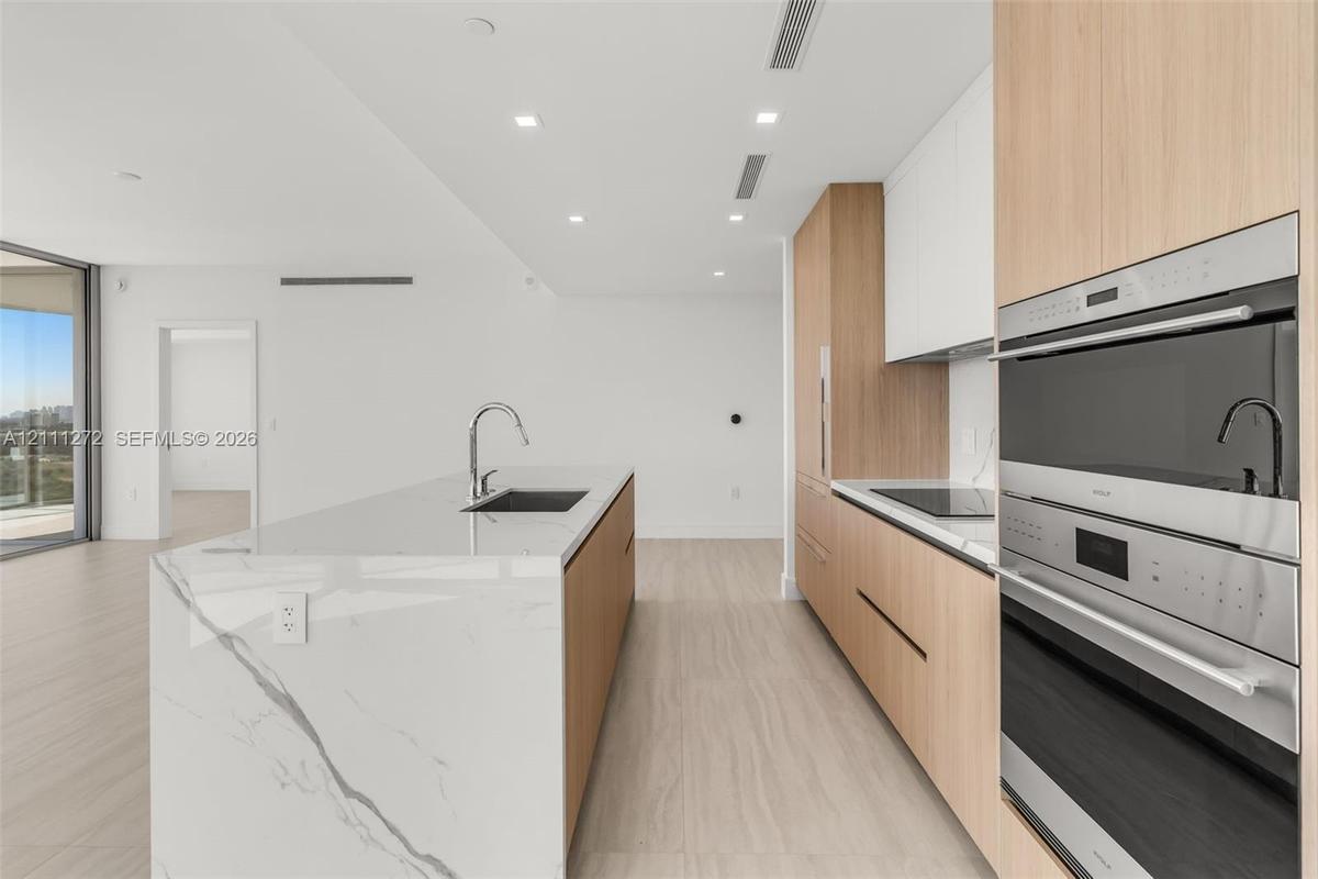 Kitchen featuring a waterfall-edge island with stone-finish countertops, wood-finish cabinetry, built-in stainless steel wall ovens, wood-finish floor