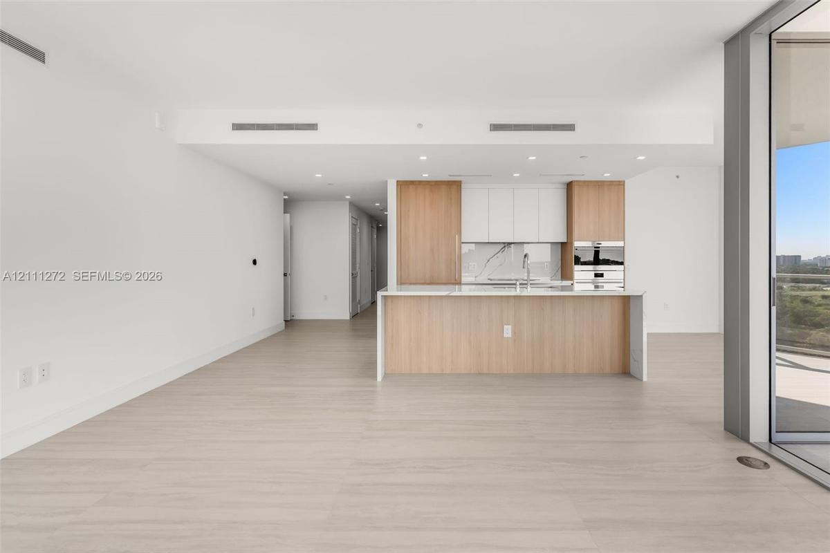 Kitchen featuring two-tone wood-finish and white cabinetry, stone-finish backsplash, built-in stainless steel appliances, and a central island with a 