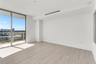 Floor-to-ceiling glass sliding doors, wood-finish flooring, private balcony with metal railing, and neutral wall palette