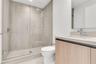 Walk-in glass-enclosed shower with large-format stone-finish tile surround, wood-finish floating vanity, integrated rectangular basin, and wall-to-wal