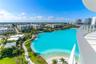Private balcony with glass panel railing overlooking a large turquoise lagoon, paved walking paths, and landscaped green space