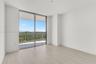 Floor-to-ceiling sliding glass door, light-toned wood-finish flooring, and covered balcony with metal railing
