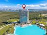 High-rise residential tower featuring a glass facade, situated on a waterfront lot with an expansive turquoise lagoon, surrounded by established green