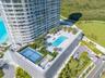 Elevated amenity deck featuring a swimming pool, tennis court, manicured landscaping, and structured parking
