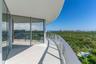 Curved wrap-around balcony featuring large-format tile flooring, floor-to-ceiling glass sliding doors, and a transparent glass railing