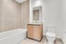 Bathroom featuring floor-to-ceiling textured tile surround, built-in vanity with wood-finish cabinetry, countertop basin, rectangular wall-mounted mir